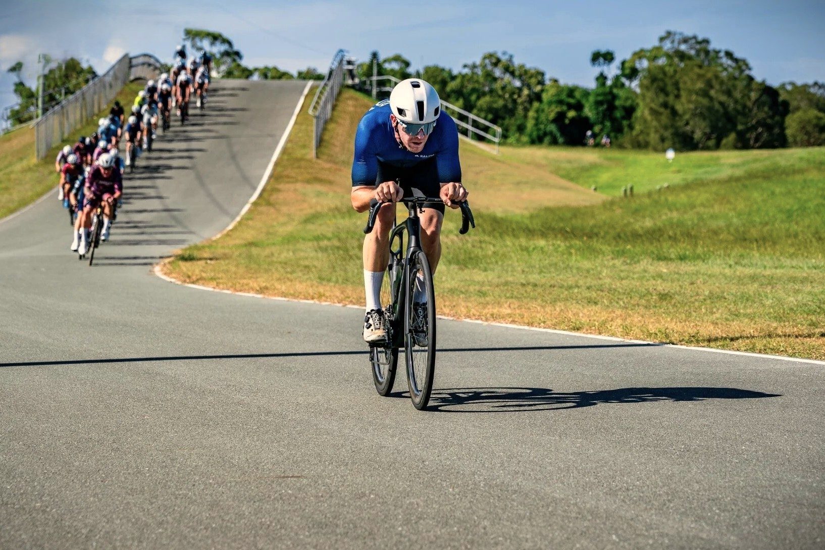 A cyclist riding clear off the front of the race, the field strung out on the hill behind